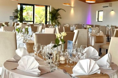 Salle de réception élégamment décorée avec des tables rondes dressées, nappes blanches et centres de table floraux.
