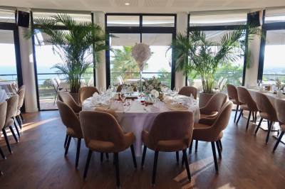 Salle de réception élégamment décorée avec des tables rondes dressées, nappes blanches et centres de table floraux.
