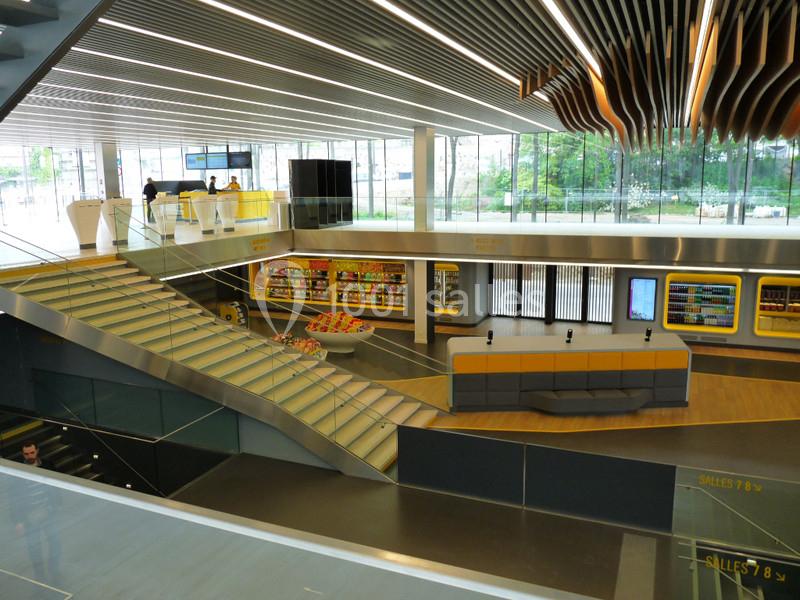 Intérieur moderne avec escalier, coin salon, étagères de produits et grandes baies vitrées donnant sur l'extérieur.