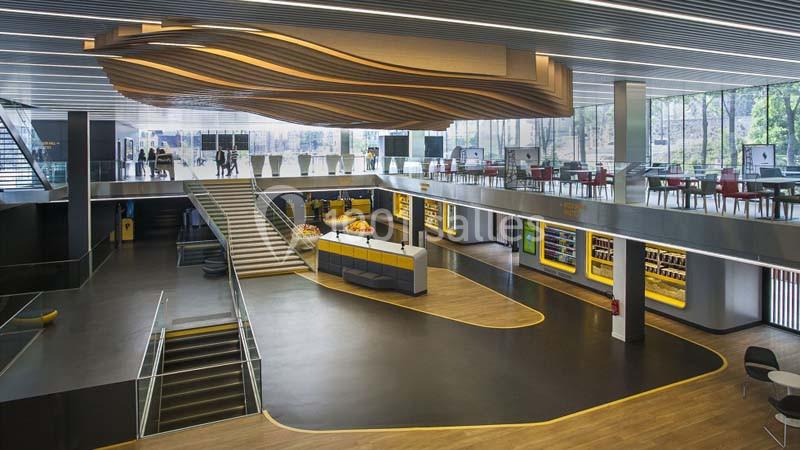 Hall moderne avec escalier central, plafond ondulé en bois, espaces ouverts, vitrines et lumière naturelle abondante.