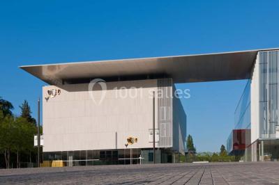 Bâtiment moderne avec façade blanche, toit en surplomb et grandes baies vitrées, entouré de végétation.
