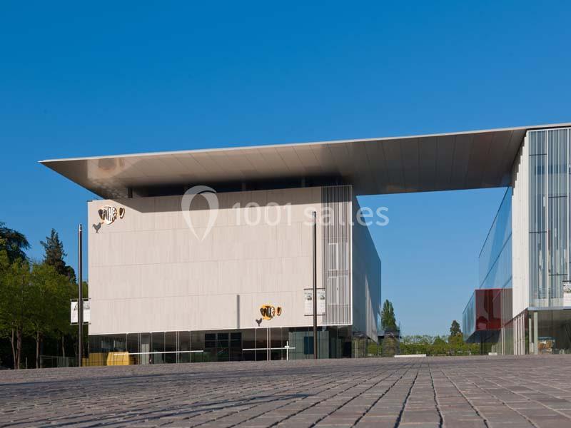 Bâtiment moderne avec façade blanche, toit en surplomb et grandes baies vitrées, entouré de végétation.