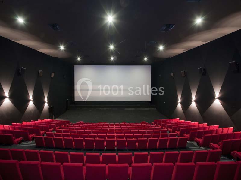 Salle de cinéma vide avec des rangées de sièges rouges et un grand écran blanc éclairé.
