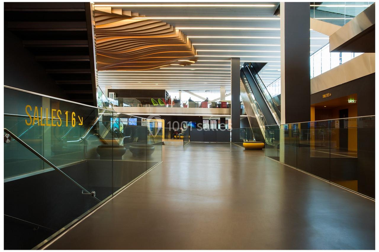 Intérieur moderne avec escalators, escalier, plafond ondulé et signalisation des salles dans un espace lumineux.
