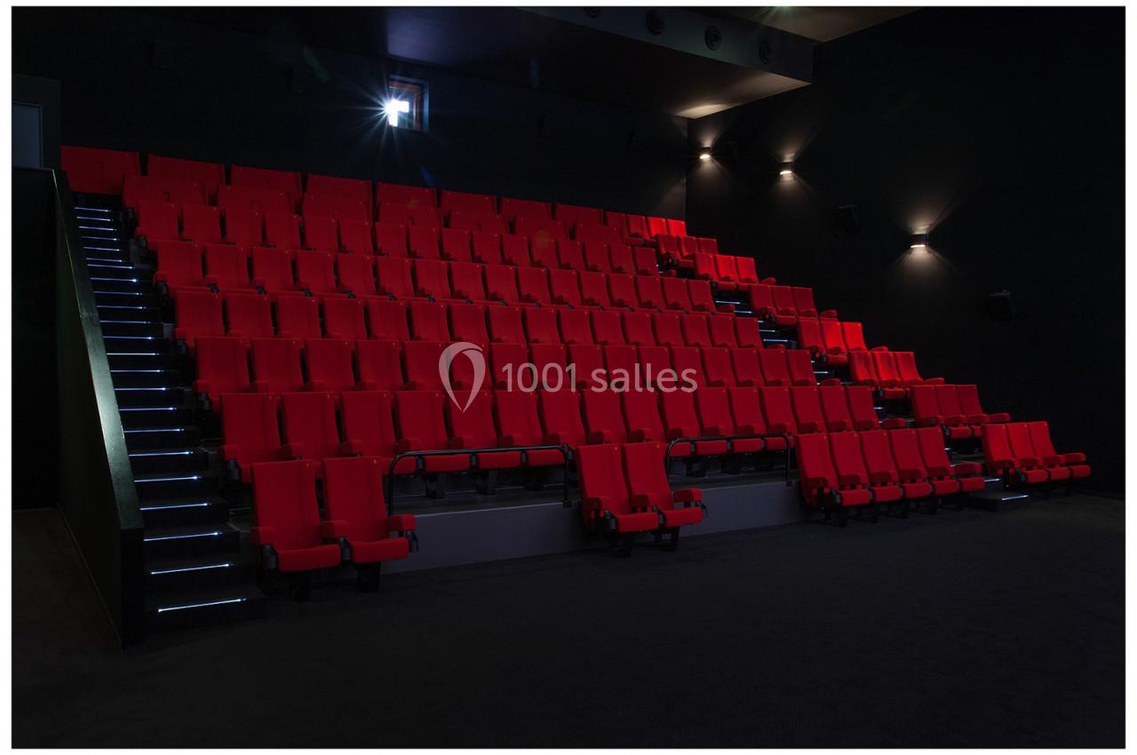 Salle de cinéma vide avec des rangées de sièges rouges et un éclairage tamisé.