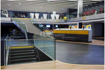 Bâtiment moderne avec façade blanche, toit en surplomb et grandes baies vitrées, entouré de végétation.