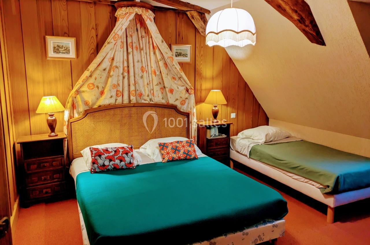 Chambre avec un lit double et un lit simple, décorée de bois, avec des lampes de chevet et un plafond mansardé.