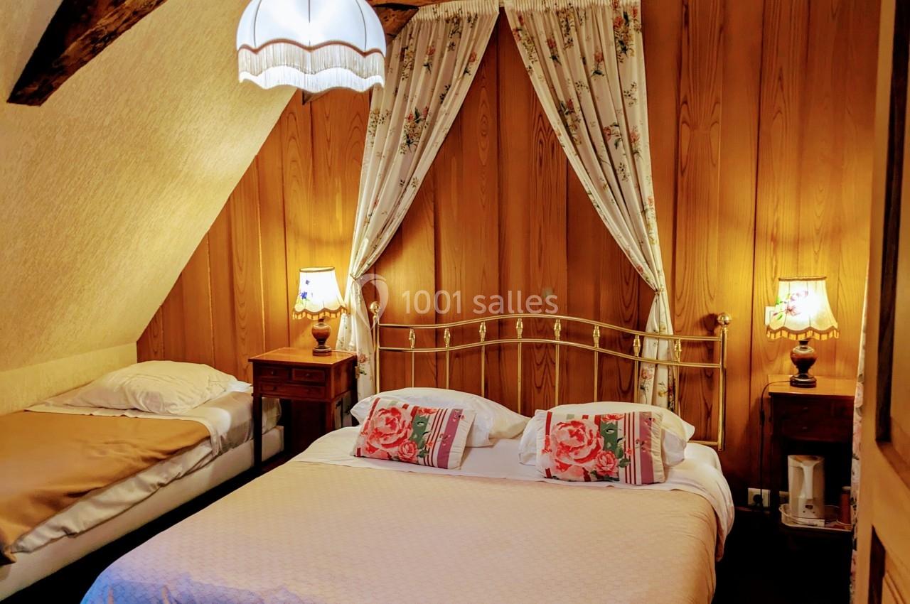 Chambre avec lit double et lit simple, poutres apparentes, murs en bois, lampes de chevet et rideaux fleuris.
