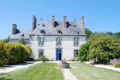 Salon avec plafond en poutres apparentes, mobilier ancien, canapé, fauteuils et éclairage chaleureux.