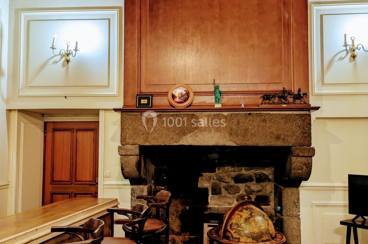 Cheminée en pierre dans une pièce avec plafond en poutres apparentes, bar en bois et globe terrestre au premier plan.