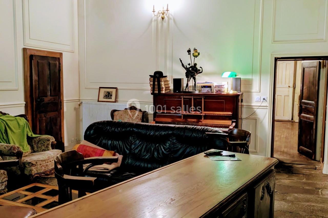 Salon avec plafond en poutres apparentes, mobilier ancien, canapé, fauteuils et éclairage chaleureux.