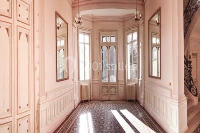 Grande maison en pierre blanche entourée d'arbres, avec une allée et un jardin ensoleillé à l'avant.