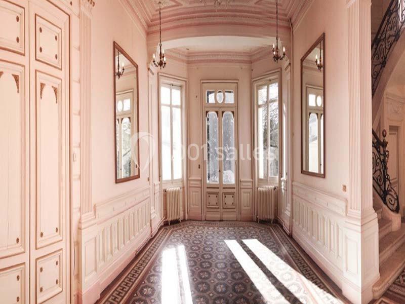 Intérieur lumineux d'une pièce ancienne avec moulures, grandes fenêtres, miroirs et sol en carreaux décoratifs.