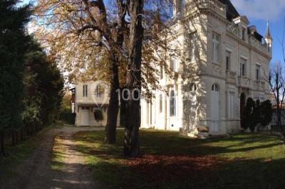 Grande maison en pierre blanche entourée d'arbres, avec une allée et un jardin ensoleillé à l'avant.