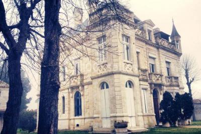 Grande maison en pierre blanche entourée d'arbres, avec une allée et un jardin ensoleillé à l'avant.