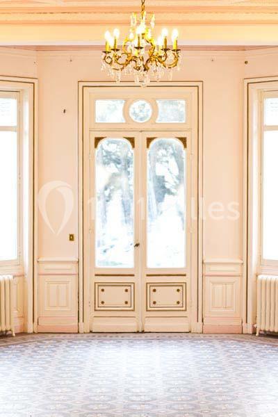 Porte-fenêtre ancienne avec vitraux, encadrée par deux radiateurs, dans une pièce lumineuse au sol carrelé.