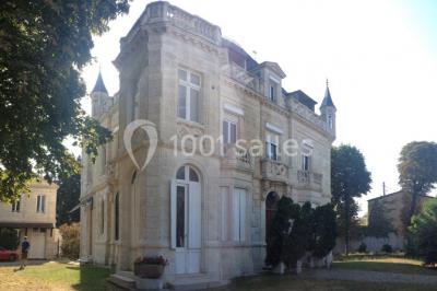 Grande maison en pierre blanche entourée d'arbres, avec une allée et un jardin ensoleillé à l'avant.