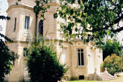 Grande maison en pierre blanche entourée d'arbres, avec une allée et un jardin ensoleillé à l'avant.