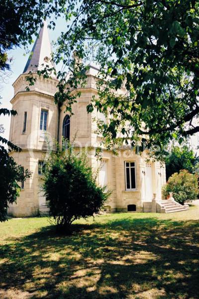 Façade d'un petit château en pierre entouré d'arbres et d'un jardin ombragé.