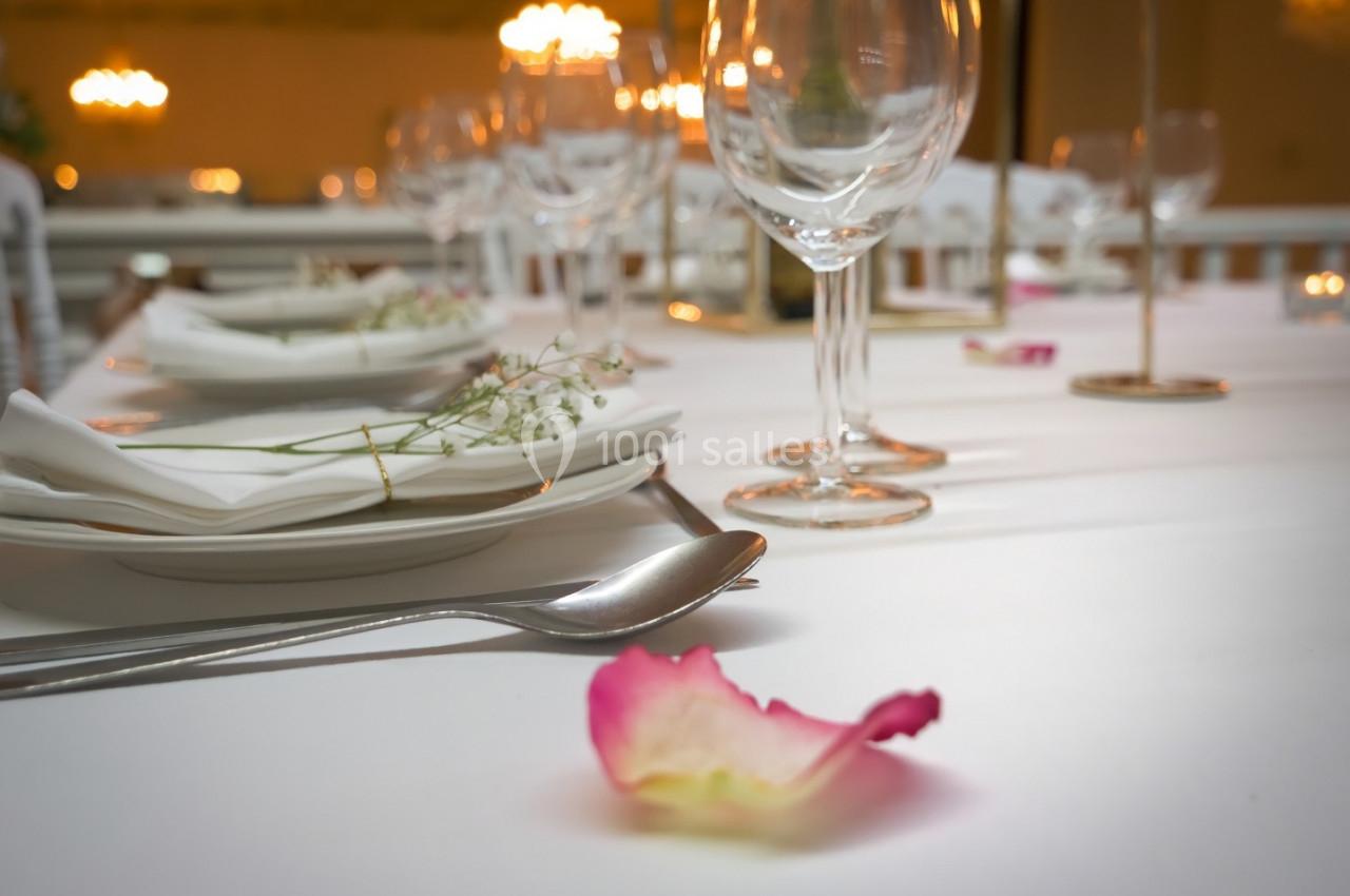 Table dressée avec des assiettes, verres et couverts, décorée de pétales de rose et de fleurs blanches.