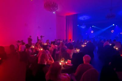Salle tamisée avec des spectateurs assis à des tables éclairées par des bougies, face à une scène illuminée en rouge et bleu.