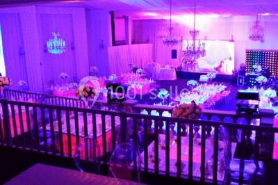 Salle de réception décorée avec des tables dressées, des chaises transparentes et un éclairage violet.