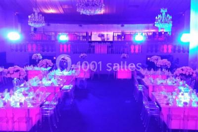 Salle de réception décorée avec des tables dressées, des chaises transparentes et un éclairage violet.