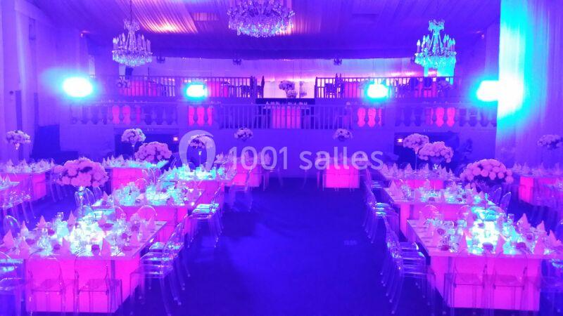 Salle de réception décorée avec des tables illuminées en rose, des chaises transparentes et des fleurs blanches.