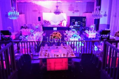 Salle de réception décorée avec des tables dressées, des chaises transparentes et un éclairage violet.