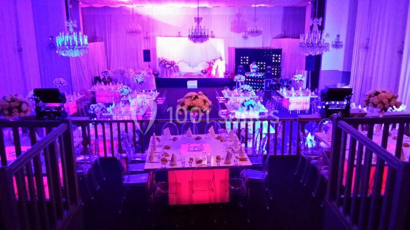 Salle de réception décorée avec des tables illuminées, des chandeliers suspendus et une scène en arrière-plan.