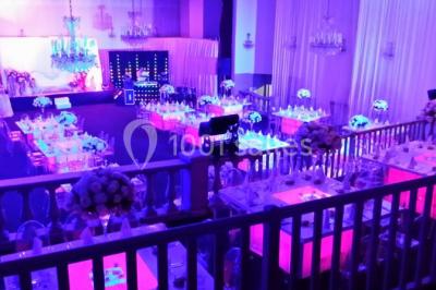 Salle de réception décorée avec des tables dressées, des chaises transparentes et un éclairage violet.