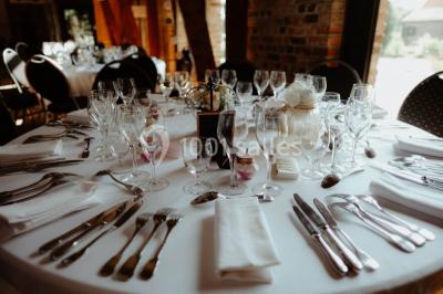 Table élégamment dressée avec menu, couverts, verres et une fleur rouge en centre de table, éclairée par la lumière…