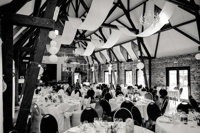 Salle de réception avec poutres apparentes, tables dressées et décorations suspendues dans un style élégant.
