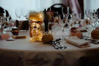 Table élégamment dressée avec menu, couverts, verres et une fleur rouge en centre de table, éclairée par la lumière…