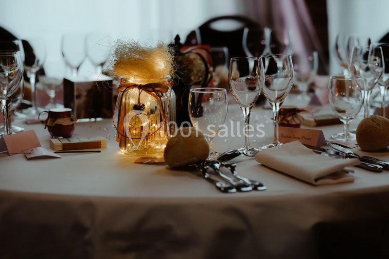 Table élégamment dressée avec des verres, couverts, serviettes et un centre de table lumineux décoratif.
