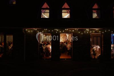 Table élégamment dressée avec menu, couverts, verres et une fleur rouge en centre de table, éclairée par la lumière…