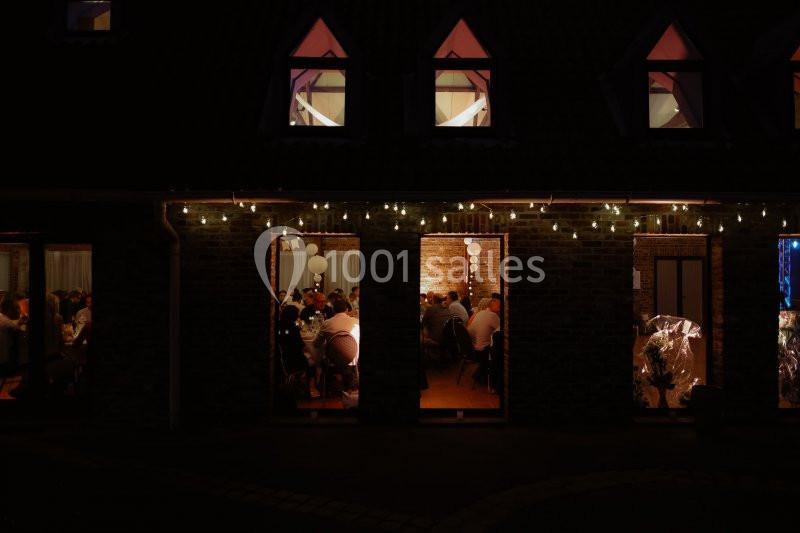 Façade d'un bâtiment en soirée avec des fenêtres éclairées laissant entrevoir des personnes réunies à l'intérieur.