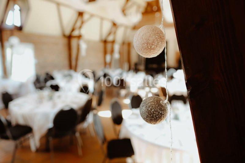 Décoration lumineuse suspendue avec des boules en fil tressé, en arrière-plan une salle de réception avec tables dressées.