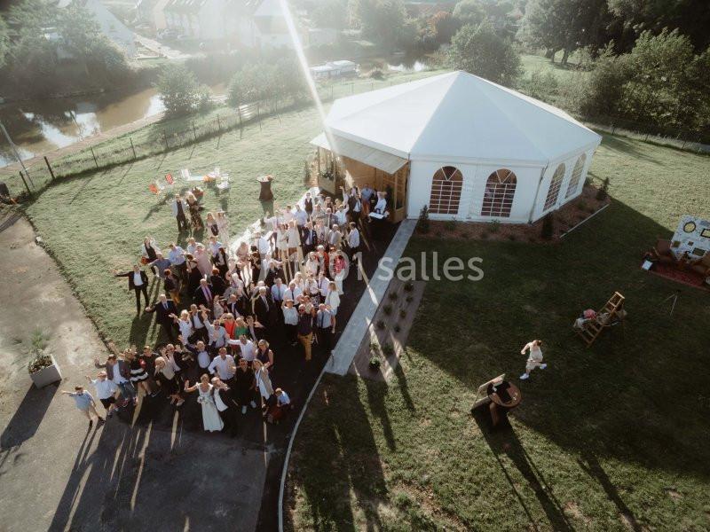 Vue aérienne d'un groupe de personnes rassemblées près d'une tente blanche dans un espace extérieur verdoyant.