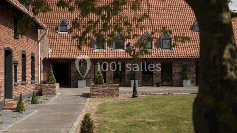 Cour intérieure d'une bâtisse en briques rouges avec toit en tuiles, arbres et arbustes décoratifs.