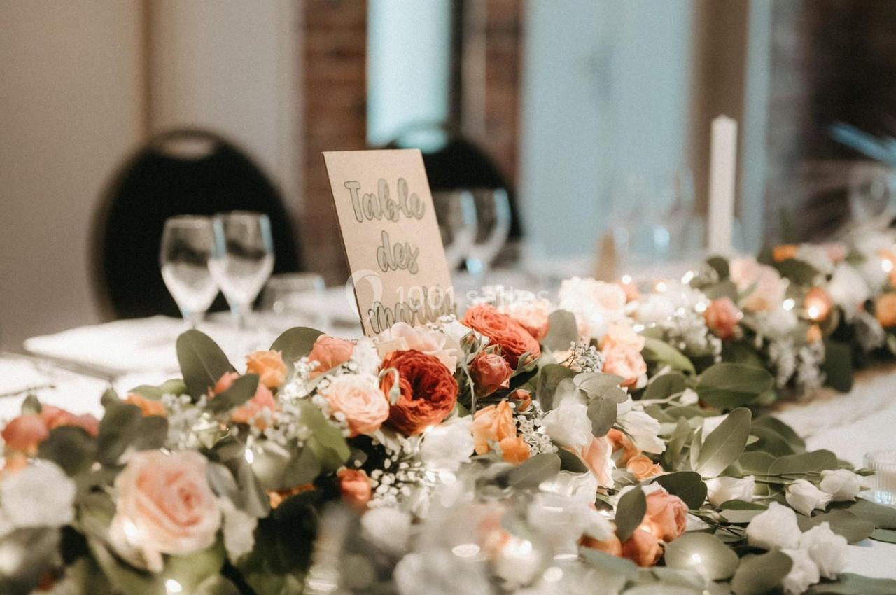Décoration de table avec un centre de table floral composé de roses et feuillage, dans une salle aux murs en briques.