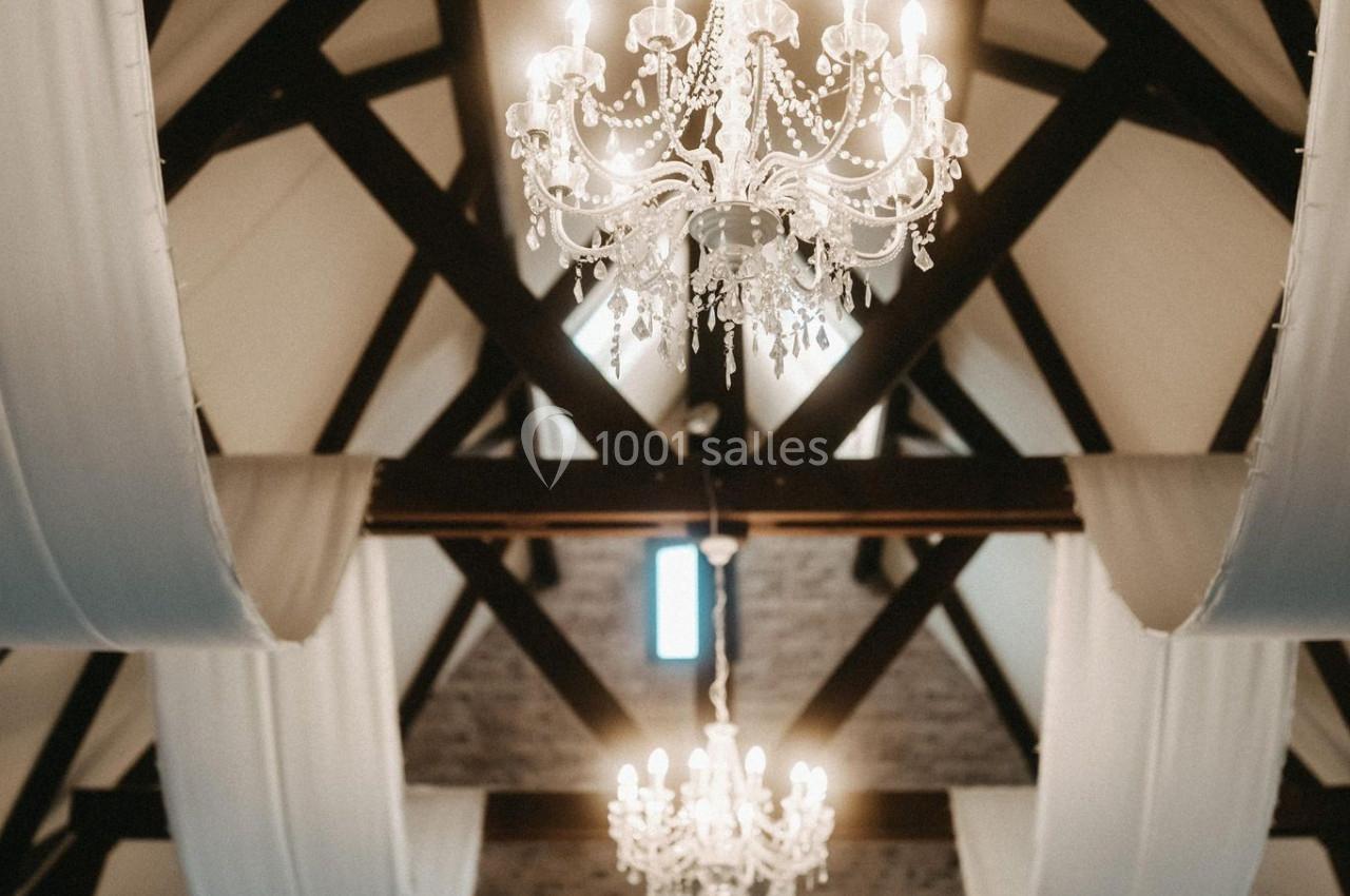Plafond avec poutres apparentes, lustres en cristal allumés et drapés blancs suspendus dans une salle élégante.