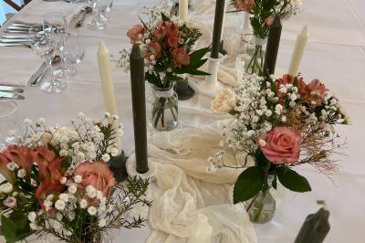 Table élégamment dressée avec menu, couverts, verres et une fleur rouge en centre de table, éclairée par la lumière…