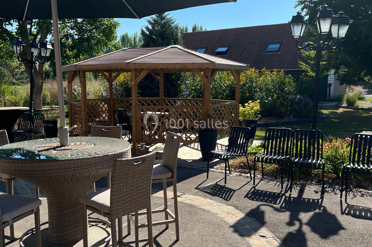 Terrasse ensoleillée avec table, chaises, parasol et pergola en bois dans un jardin verdoyant.