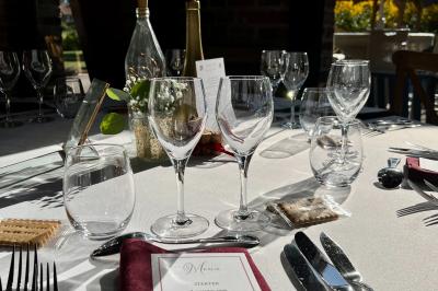 Table élégamment dressée avec menu, couverts, verres et une fleur rouge en centre de table, éclairée par la lumière…
