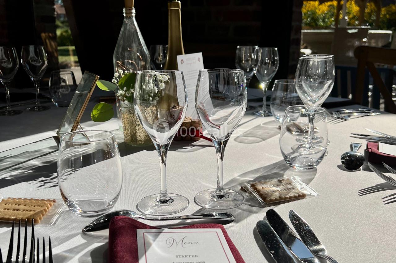 Table élégamment dressée avec menu, couverts, verres et une fleur rouge en centre de table, éclairée par la lumière…