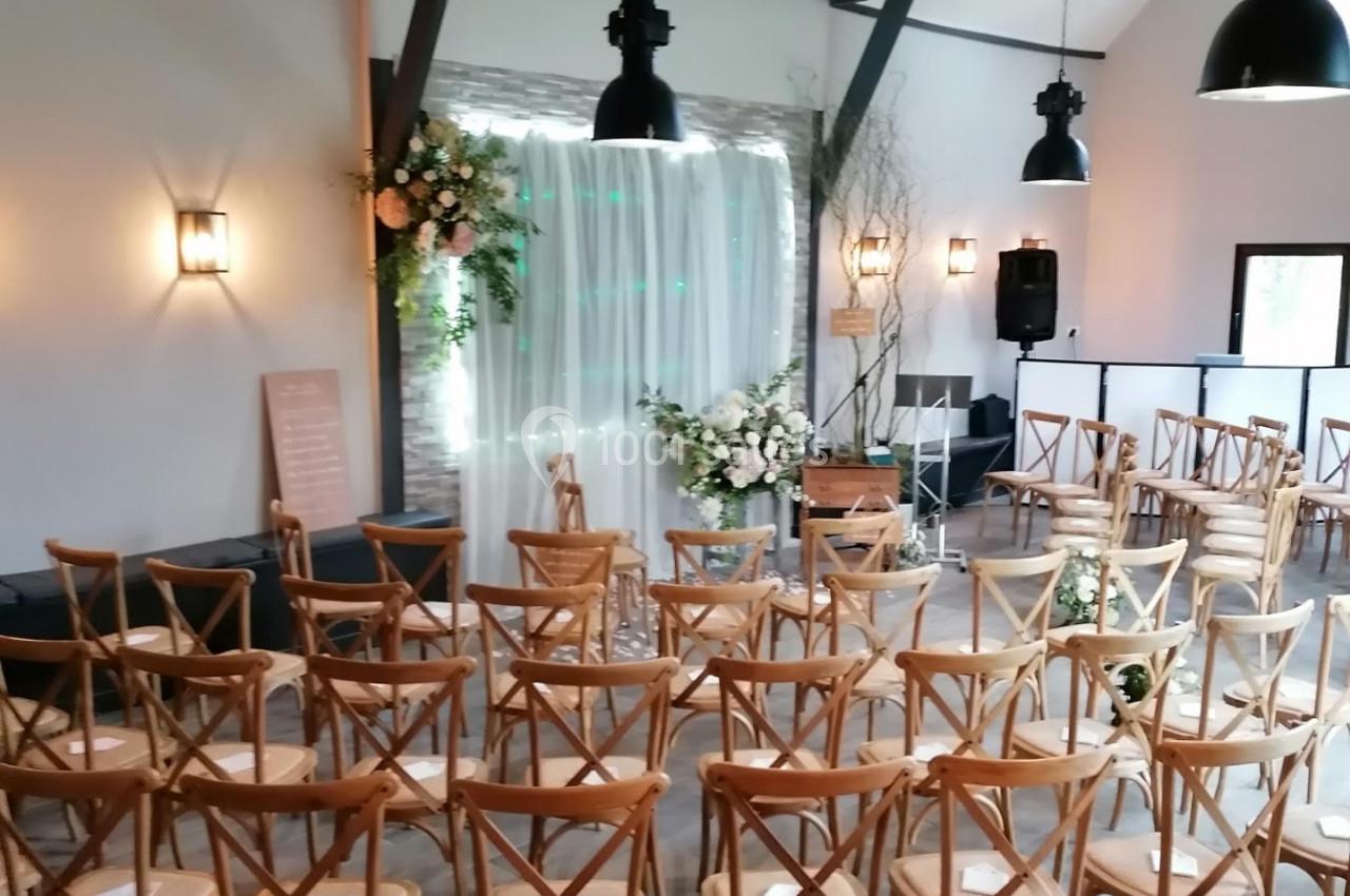 Salle de réception décorée pour une cérémonie, avec des chaises en bois disposées face à une arche fleurie.