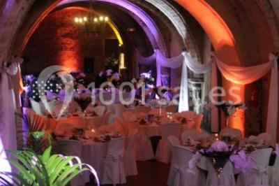 Château en pierre éclairé par des lampadaires au crépuscule, entouré d'arbres et d'une allée gravillonnée.