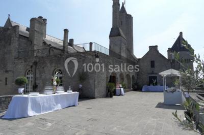 Château en pierre éclairé par des lampadaires au crépuscule, entouré d'arbres et d'une allée gravillonnée.