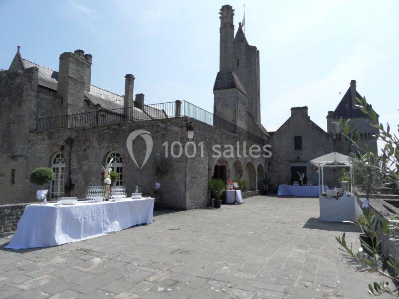 Terrasse en pierre d'un château ancien avec tables dressées pour un événement sous un ciel dégagé.